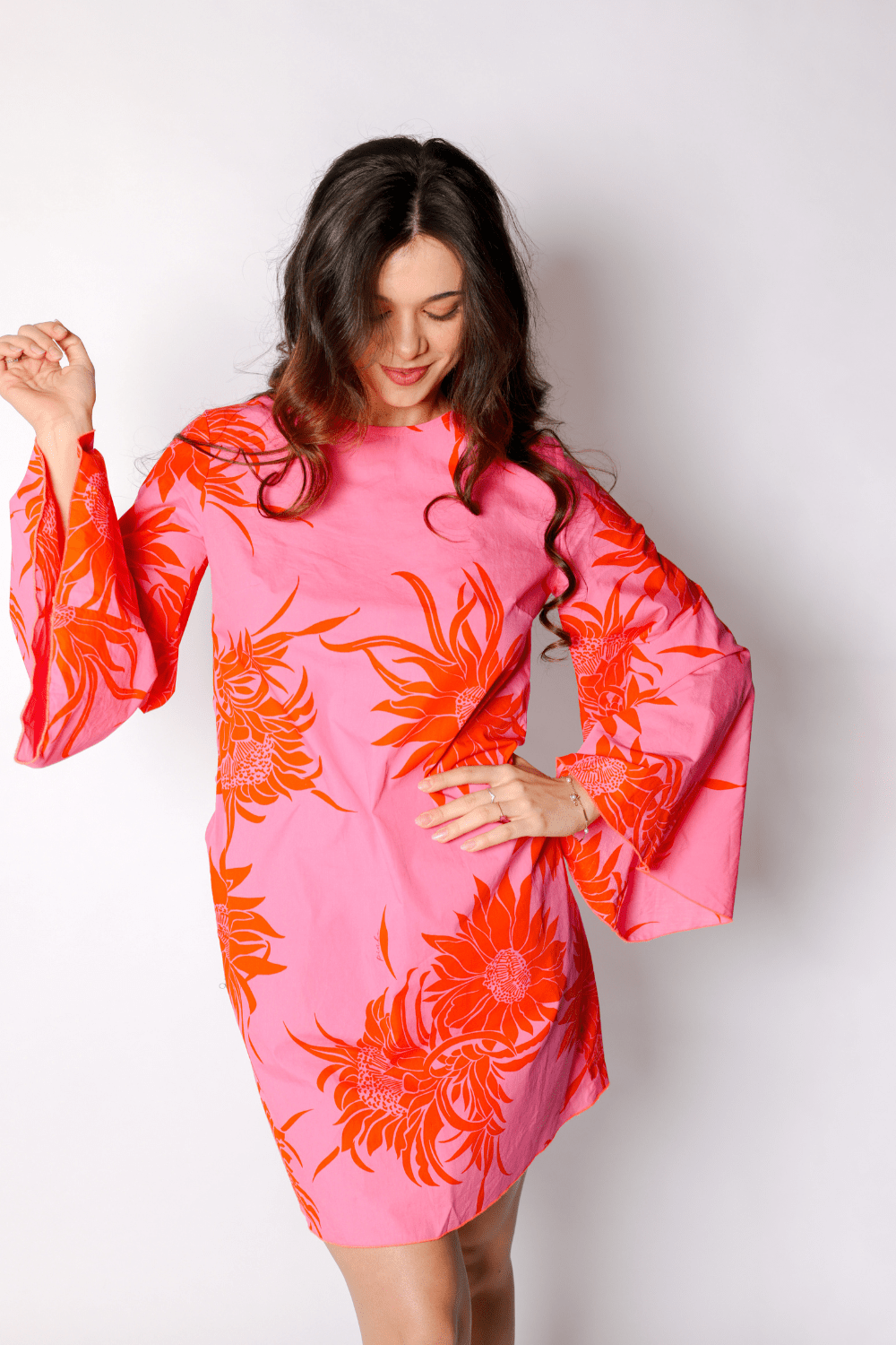 Robe mini coupe droite rétro en popeline de coton légère rose vif, grand imprimé floral orange façon tournesol oversized, manches longues extra-évasées style kimono, encolure bateau arrondie. Robe femme été colorée et élégante, made in France par Carlis.