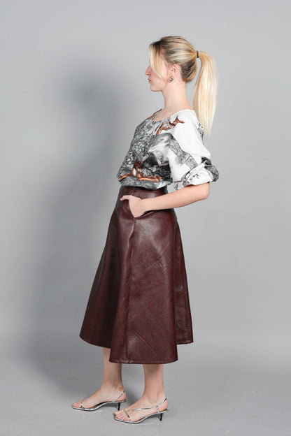 Vue de profil de la blouse Audrey en popeline de coton italien. Coupe fluide et volume moderne mettant en valeur le tombé du tissu. Manches 3/4 bouffantes élastiquées et imprimé animalier exclusif sur fond noir. Silhouette élégante associée à une jupe en cuir.