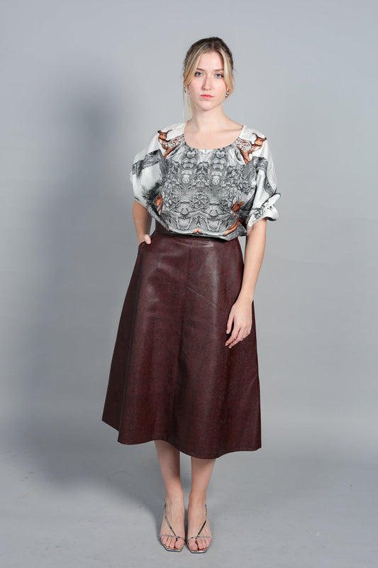 Blouse Audrey en popeline de coton italien avec imprimé jungle exclusif. Portée avec une jupe crayon en cuir bordeaux. Coupe fluide, manches 3/4 bouffantes et poignets boutonnés d'or. Fabrication artisanale française