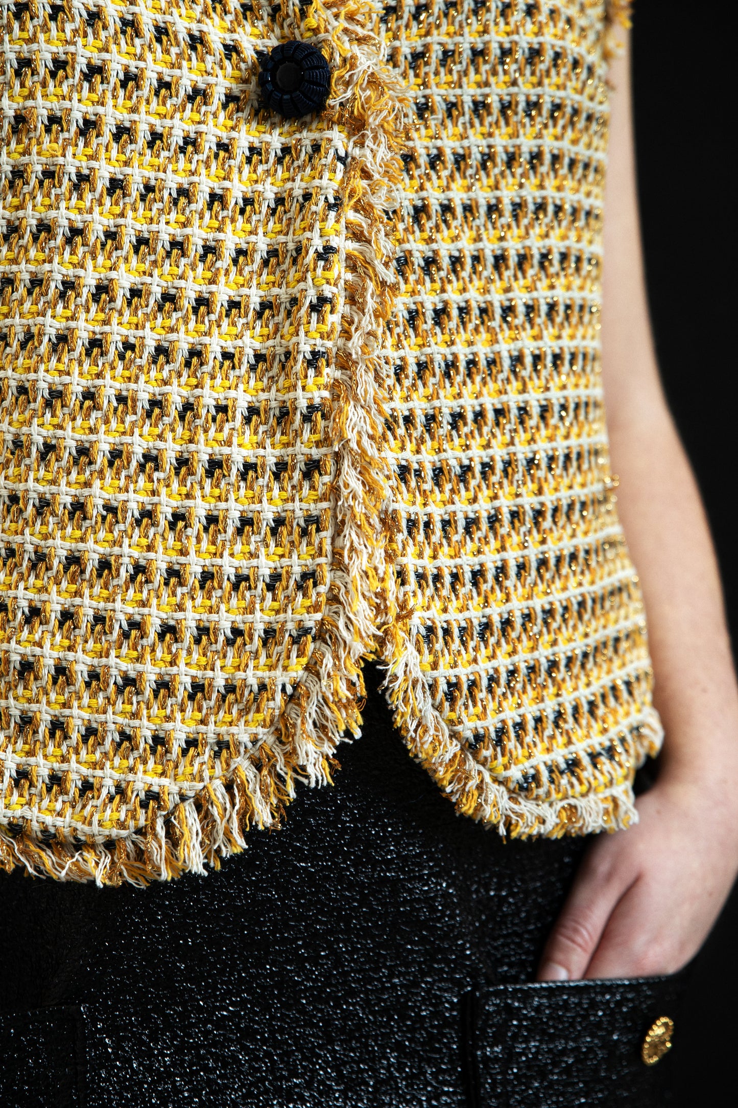 Détail finition franges artisanales bas du gilet Pole Express, tweed de coton luxe jaune et crème tissé main, bouton signature noir, confectionné en France