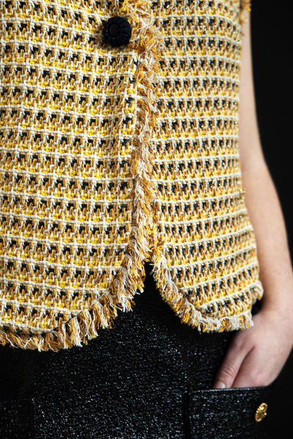 Détail finition franges artisanales bas du gilet Pole Express, tweed de coton luxe jaune et crème tissé main, bouton signature noir, confectionné en France