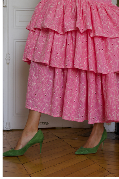 Zoom sur les volants et les chaussures : Gros plan sur les deux derniers grands volants de la robe longue rose, associés à une paire d'escarpins verts contrastants. Look chic et original.