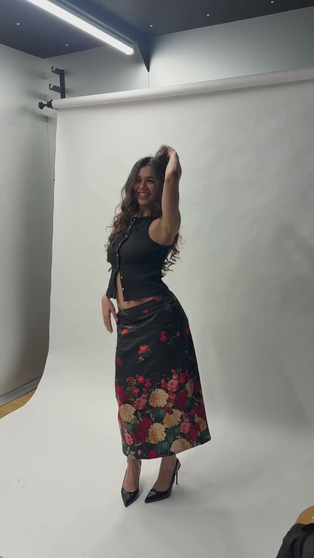 Look complet avec la jupe midi Toscane Carlis — associée à un crop top noir ajusté et des escarpins vernis, imprimé roses botaniques sur satin de coton noir. Tenue soirée ou mariage invitée, made in France.