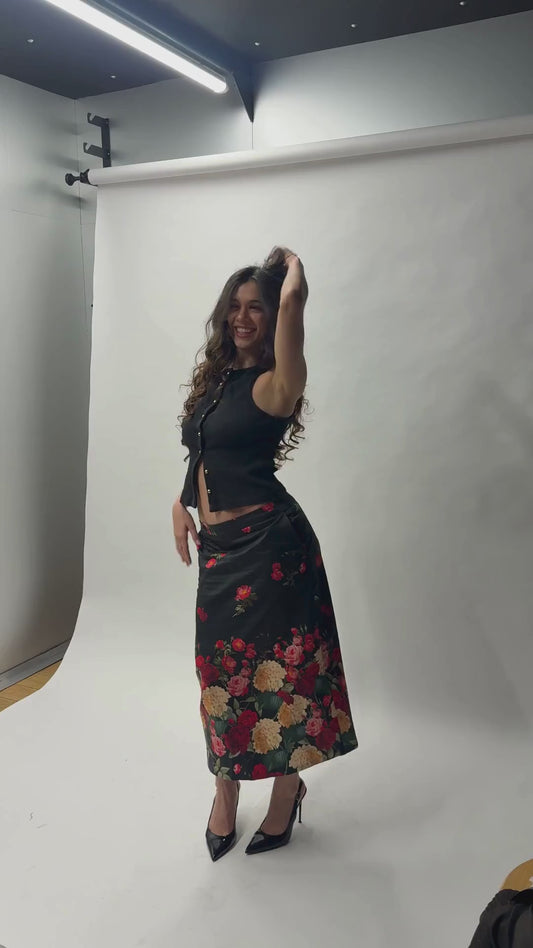 Look complet avec la jupe midi Toscane Carlis — associée à un crop top noir ajusté et des escarpins vernis, imprimé roses botaniques sur satin de coton noir. Tenue soirée ou mariage invitée, made in France.