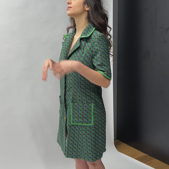 Robe courte trapèze en jacquard de coton italien, imprimé géométrique vert forêt et bleu canard, col chemisier oversize, boutonnage doré sur toute la longueur, finitions passepoil vert et poches plaquées — coupe rétro-chic inspirée des années 70, façonnée en France par Carlis
