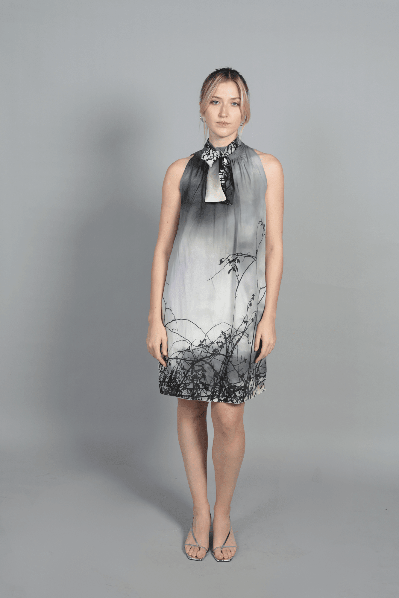 "Robe Bella Carlis en soie et viscose, coupe droite fluide avec imprimé paysage poétique gris et noir. Robe de cérémonie sans manches avec col lavallière élégant. Confection française artisanale pour un look d'invitée de mariage sophistiqué."