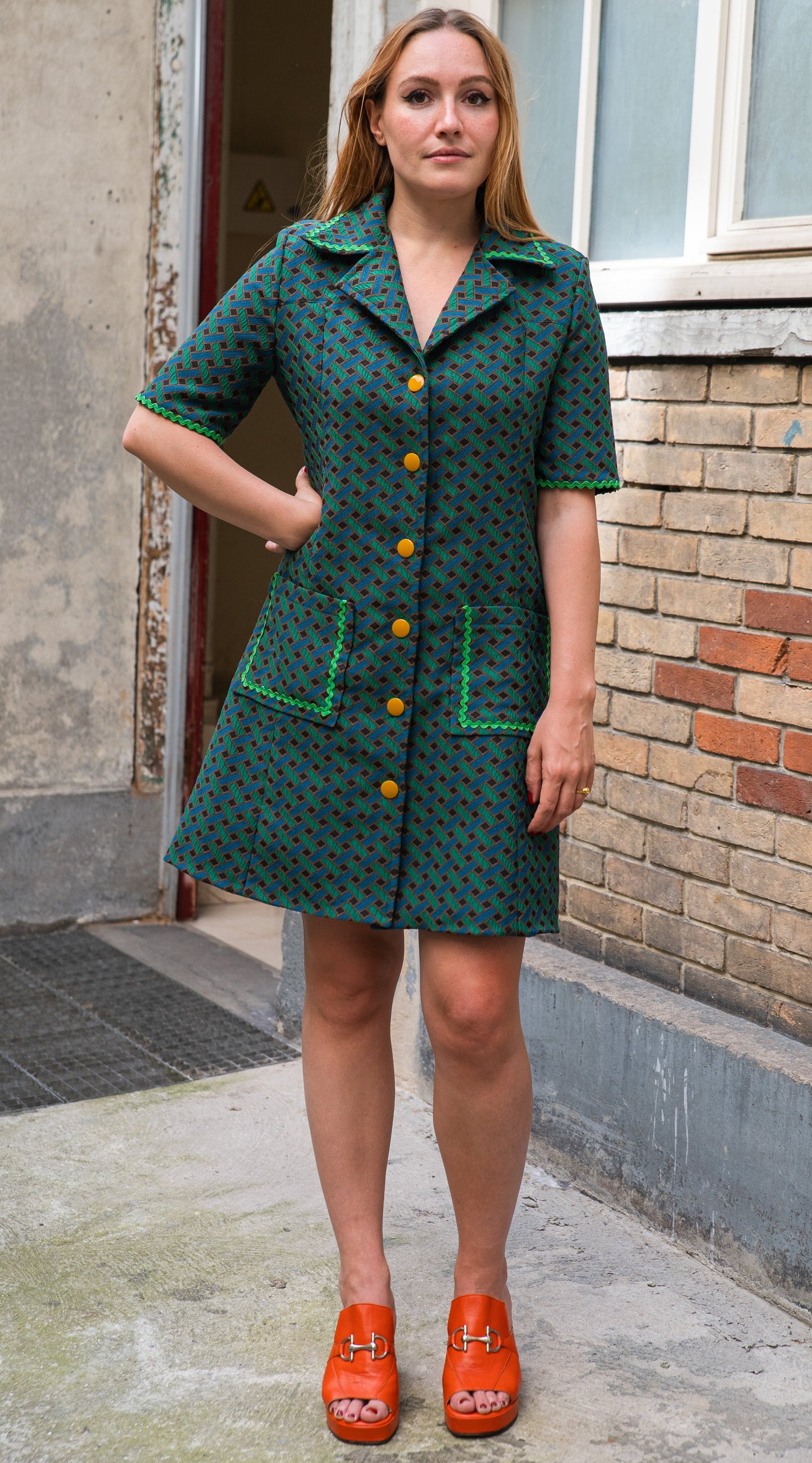Vue de face de la robe trapèze en jacquard de coton italien — imprimé géométrique vert forêt et noir, boutonnage orange sur toute la longueur, col chemisier à larges revers, manches courtes avec croquet vert, deux poches plaquées. Robe élégante femme coupe rétro années 70, made in France par Carlis.
