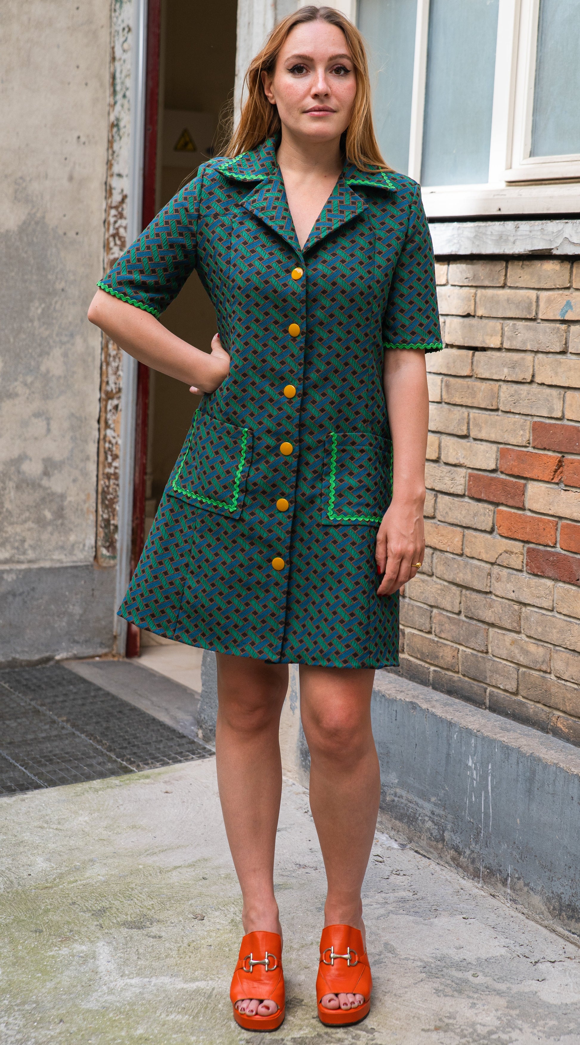 Vue de face de la robe trapèze en jacquard de coton italien — imprimé géométrique vert forêt et noir, boutonnage orange sur toute la longueur, col chemisier à larges revers, manches courtes avec croquet vert, deux poches plaquées. Robe élégante femme coupe rétro années 70, made in France par Carlis.
