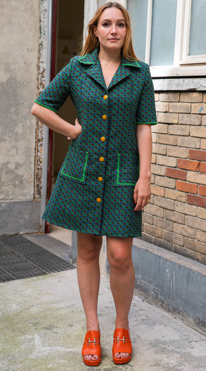 Vue de face de la robe trapèze en jacquard de coton italien — imprimé géométrique vert forêt et noir, boutonnage orange sur toute la longueur, col chemisier à larges revers, manches courtes avec croquet vert, deux poches plaquées. Robe élégante femme coupe rétro années 70, made in France par Carlis.
