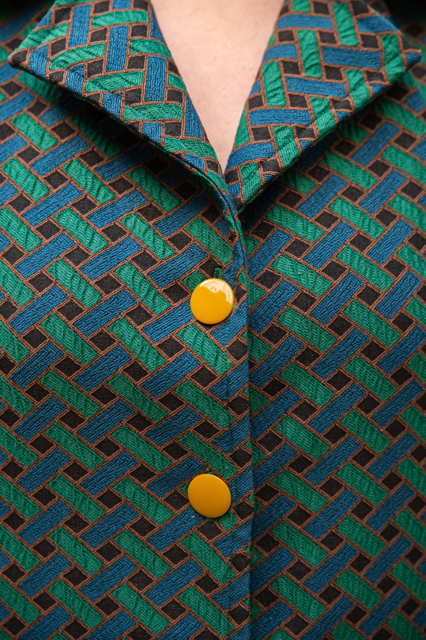 Gros plan sur le col chemisier à larges revers et les boutons ronds jaune moutarde de la robe jacquard de coton italien Carlis — tissage géométrique texturé vert forêt, bleu canard et noir, encolure V, boutonnage contrasté. Détail couture artisanale, robe élégante femme made in France.
