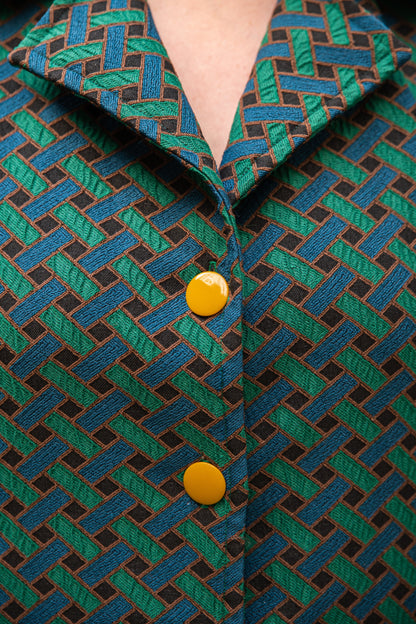 Gros plan sur le col chemisier à larges revers et les boutons ronds jaune moutarde de la robe jacquard de coton italien Carlis — tissage géométrique texturé vert forêt, bleu canard et noir, encolure V, boutonnage contrasté. Détail couture artisanale, robe élégante femme made in France.
