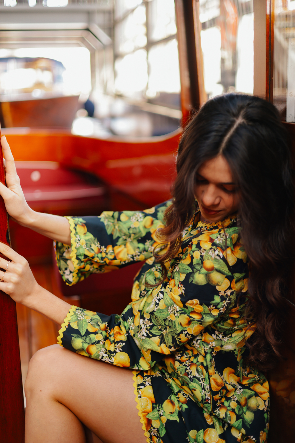 Robe courte mode femme élégante et tendance, modèle Limone. Robe d’été chic à imprimé citrons portée dans un cadre luxueux. Coupe trapèze avec manches pagode et finitions festonnées jaunes. Look idéal pour une invitée de mariage, une soirée cocktail ou un événement estival. Création haut de gamme Carlis, Made in France.